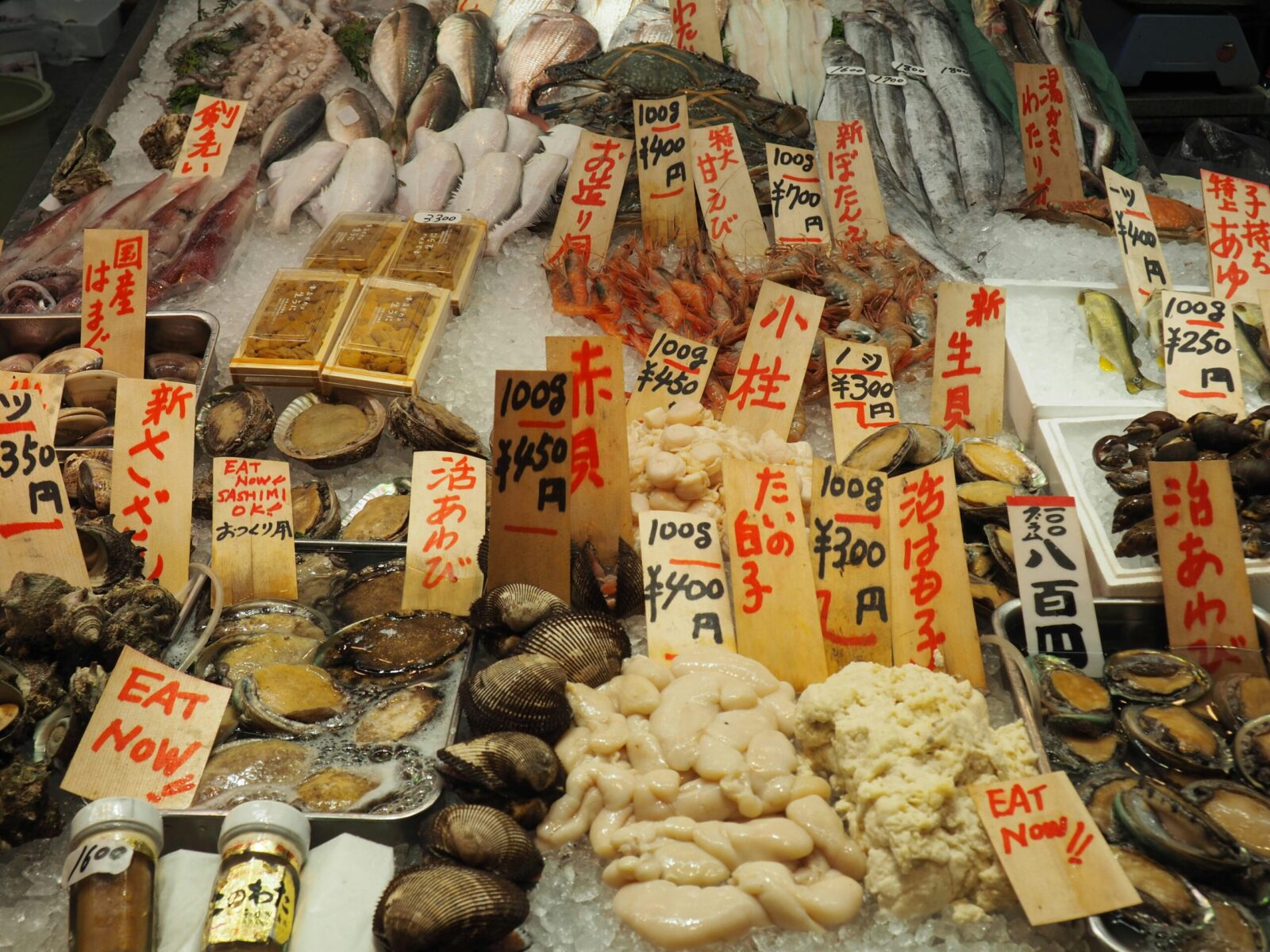 Fresh seafood assortment on ice with price tags at a bustling market stall.